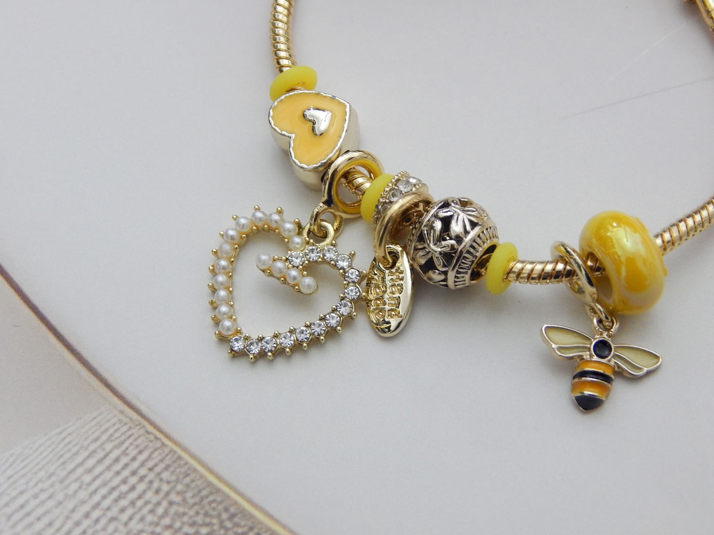 Yellow charm bracelet with bee pendant and pearl-crystal heart drop on gold chain