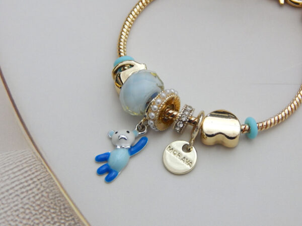 Gold-tone snake chain bracelet with blue enamel beads, teddy bear pendant, and gold heart charm