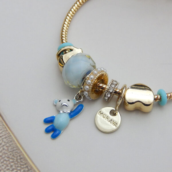 Gold-tone snake chain bracelet with blue enamel beads, teddy bear pendant, and gold heart charm