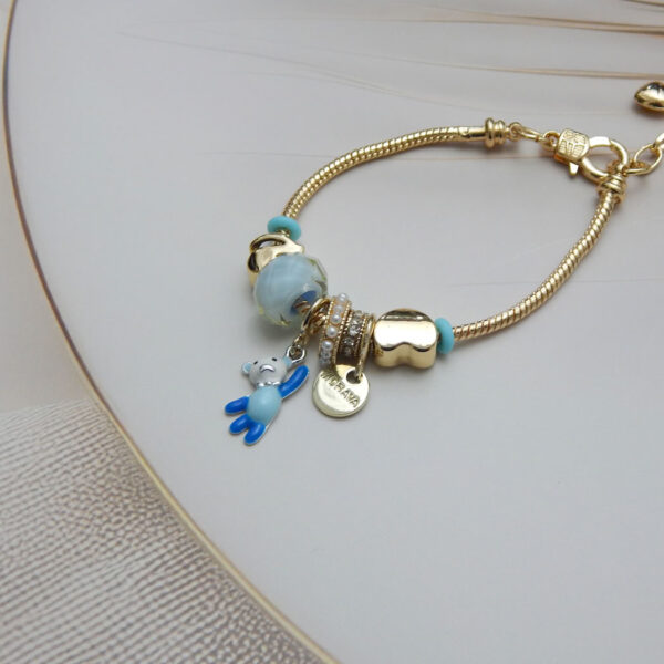 Gold-tone snake chain bracelet with blue enamel beads, teddy bear pendant, and gold heart charm