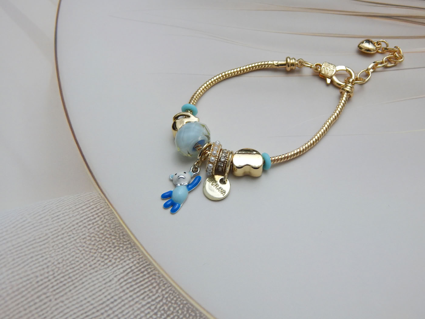 Gold-tone snake chain bracelet with blue enamel beads, teddy bear pendant, and gold heart charm