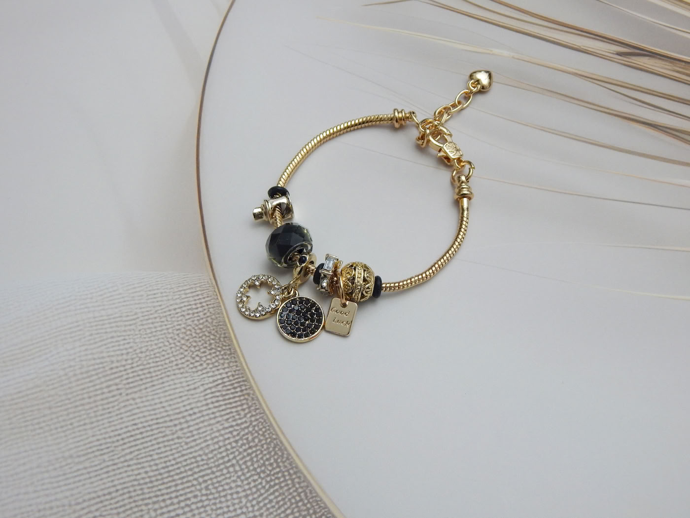 Gold-tone snake chain charm bracelet with black beads, ‘Good Luck’ tag, crystal accent charms on light background
