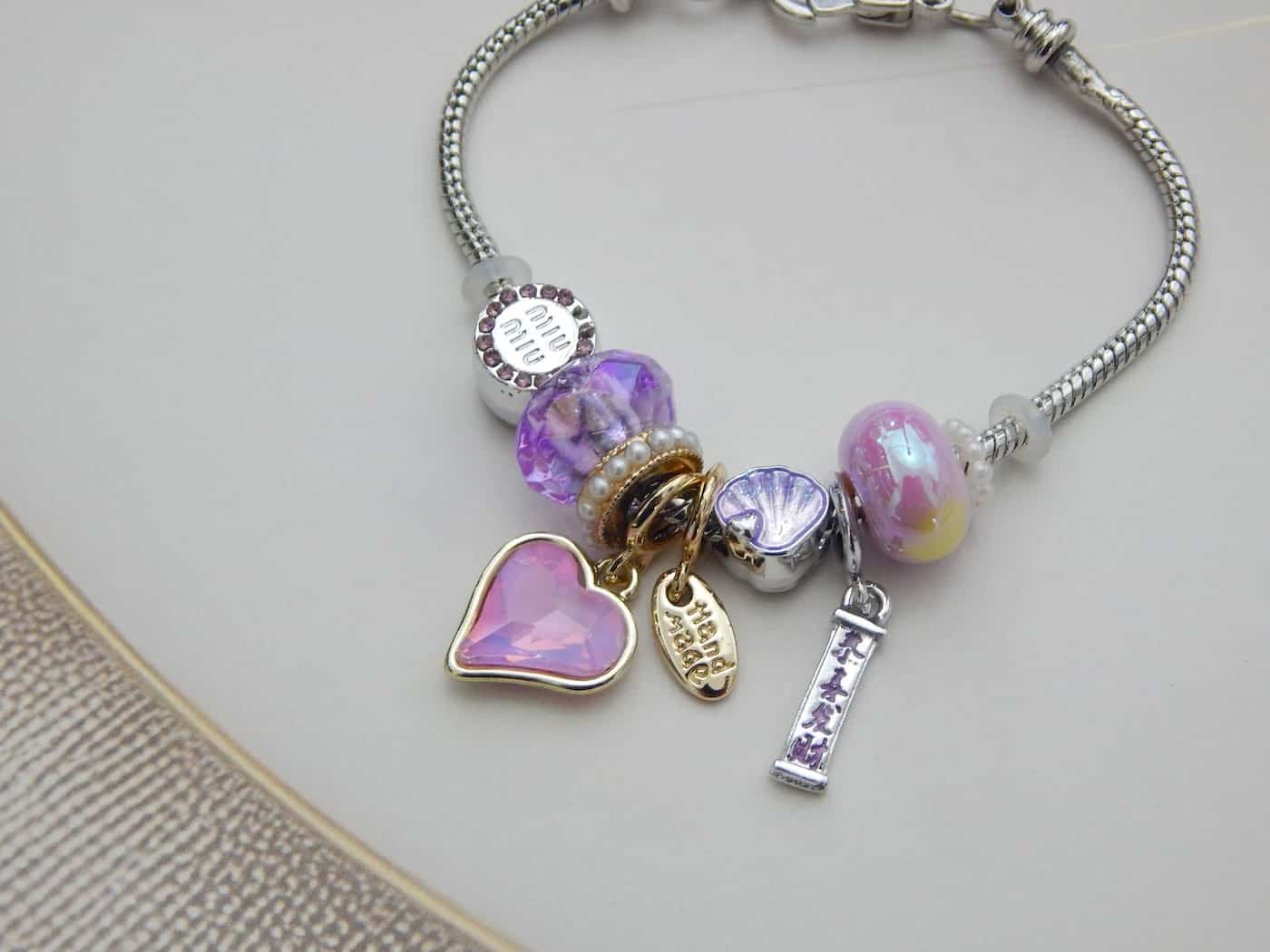 Pink Lavender Charm Bracelet with faceted heart, shell, and “Handmade” tag on silver-gold tone base