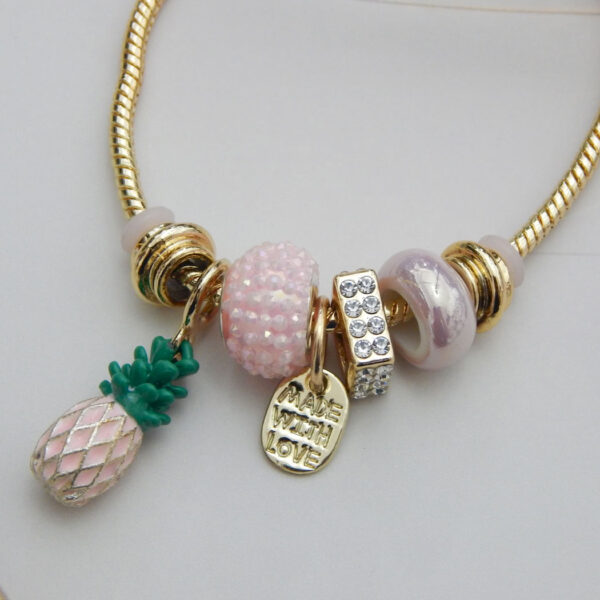 Bracelet with pink enamel pineapple charm, crystal spacer, Murano‑style beads, “Made With Love” pendant on gold snake chain