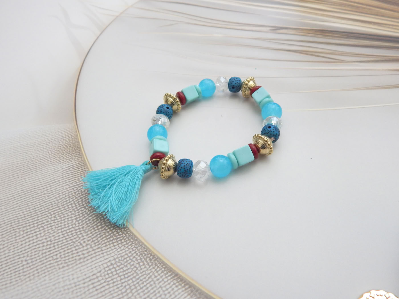 Boho-style bracelet with aqua and blue beads, red accents, and a turquoise tassel