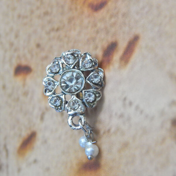 Silver crystal nath with floral stone pattern and pearl drop on textured background.