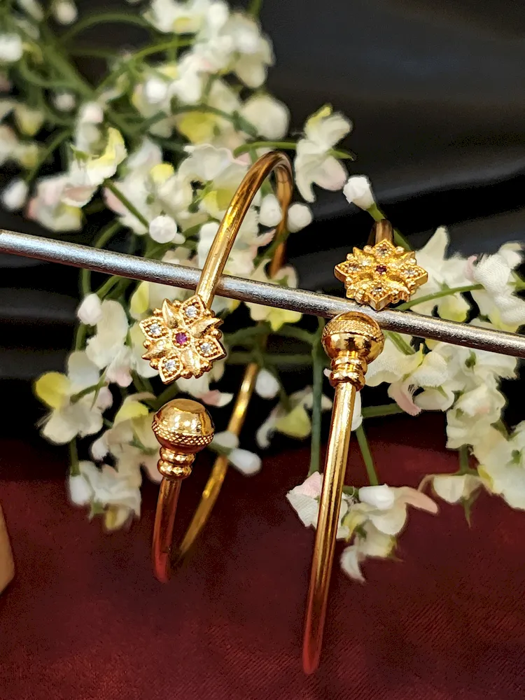 Minimalist golden kada with floral charm and ruby-accented center stone