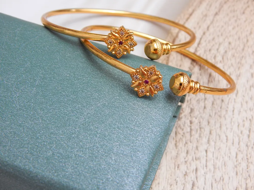 Minimalist golden kada with floral charm and ruby-accented center stone