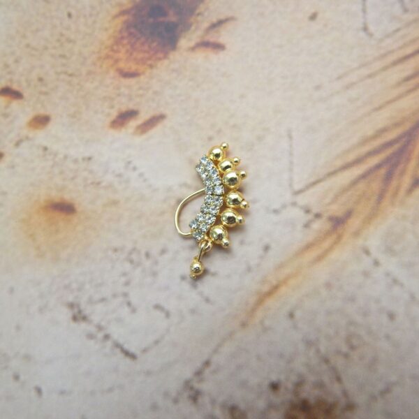 Gold-toned curve nath with white stones and ball detailing on a rustic background