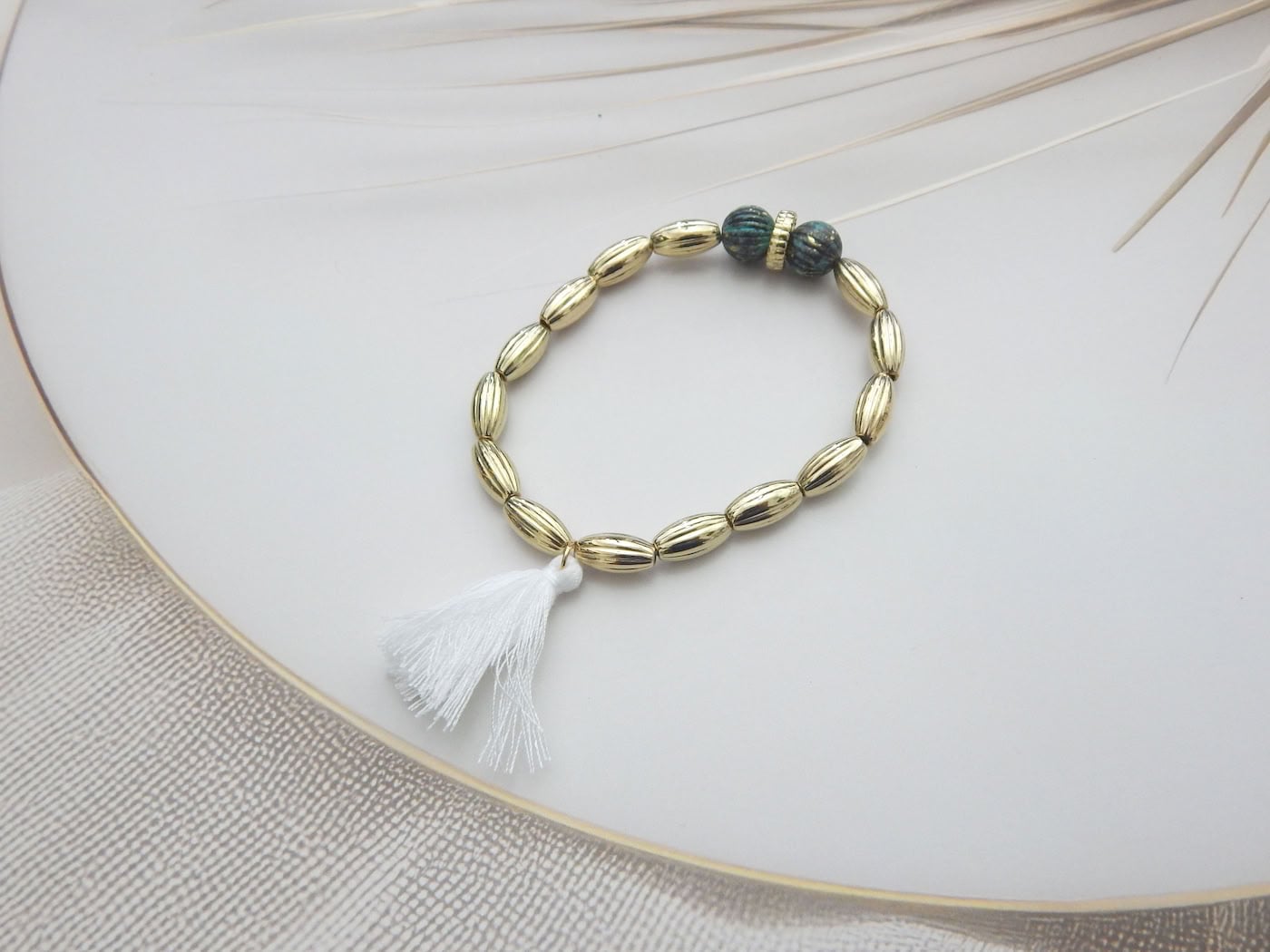 Gold oval bead bracelet with white tassel and twin textured beads