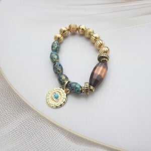 Mixed bead bracelet with golden textured beads, tribal-style blue stones, and a round engraved coin charm