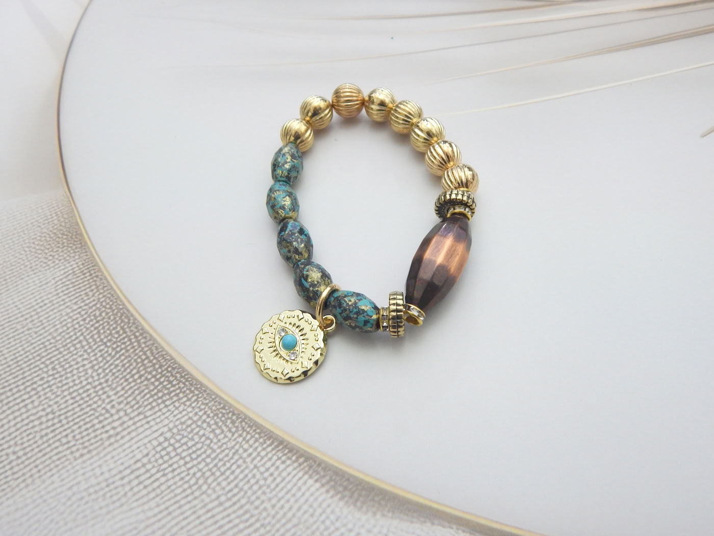 Mixed bead bracelet with golden textured beads, tribal-style blue stones, and a round engraved coin charm