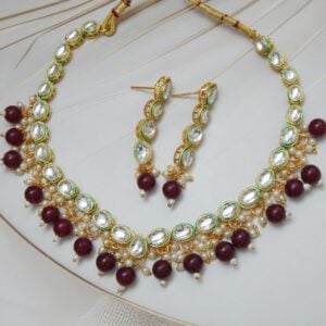 A traditional Indian Kundan Polki necklace and earring set with red beads. The design features uncut stones and gold-plated details.