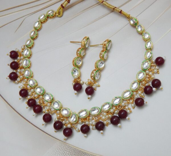 A traditional Indian Kundan Polki necklace and earring set with red beads. The design features uncut stones and gold-plated details.