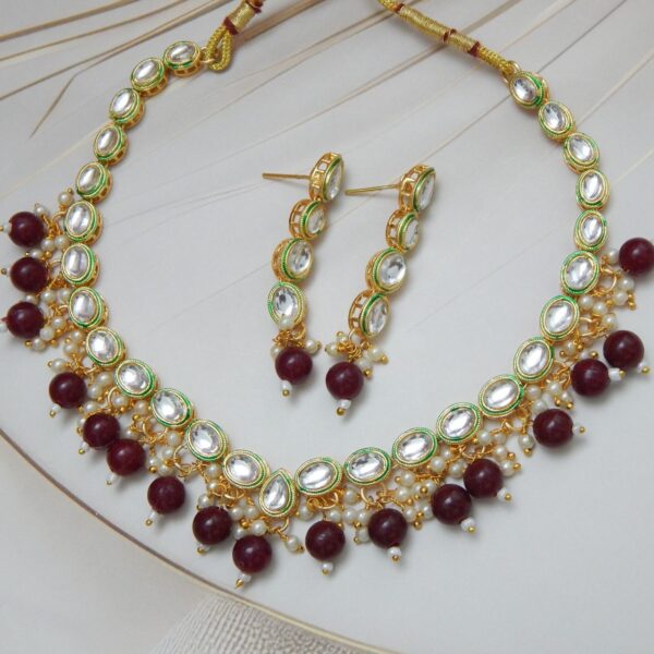 A traditional Indian Kundan Polki necklace and earring set with red beads. The design features uncut stones and gold-plated details.