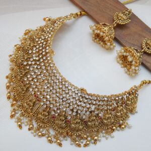 A traditional Indian temple jewelry choker and earring set with a matte gold finish, featuring AD stones, goddess motifs, and pearl drops.