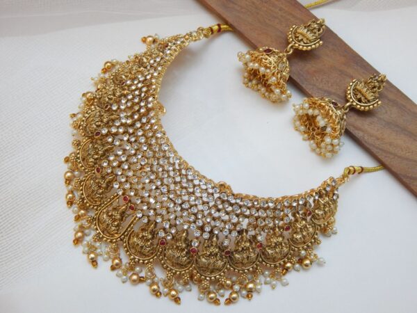 A traditional Indian temple jewelry choker and earring set with a matte gold finish, featuring AD stones, goddess motifs, and pearl drops.
