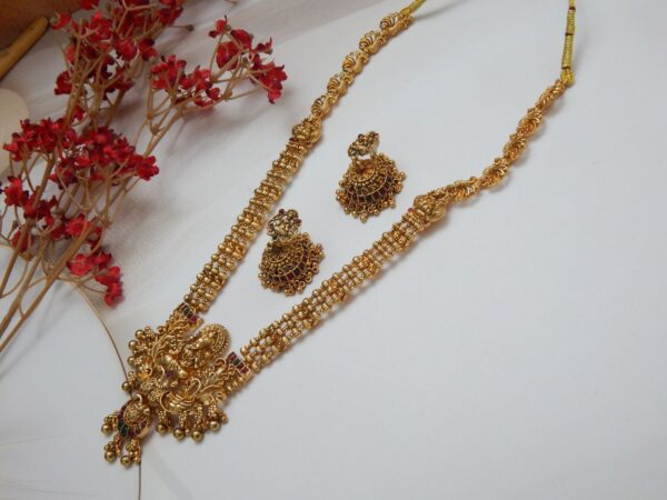 A traditional Indian temple jewelry necklace and earring set with an intricate Laxmi goddess pendant and floral designs, featuring ruby stones and cubic zirconia with a matte gold finish.