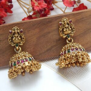 A traditional Indian temple jewelry necklace and earring set with an intricate Laxmi goddess pendant and floral designs, featuring ruby stones and cubic zirconia with a matte gold finish.