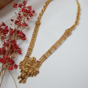 A traditional Indian temple jewelry necklace and earring set with an intricate Laxmi goddess pendant and floral designs, featuring ruby stones and cubic zirconia with a matte gold finish.