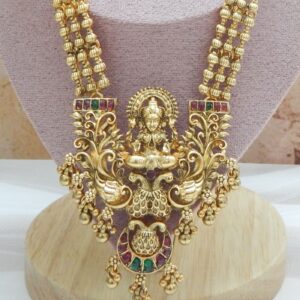 A traditional Indian temple jewelry necklace and earring set with an intricate Laxmi goddess pendant and floral designs, featuring ruby stones and cubic zirconia with a matte gold finish.