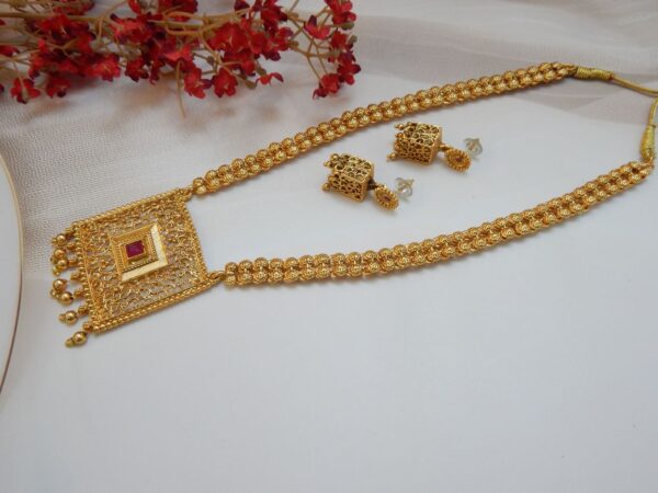 A traditional Indian long necklace with a square-shaped filigree pendant, a central red ruby stone, and matching square stud earrings with a matte gold finish.