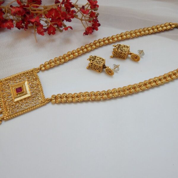 A traditional Indian long necklace with a square-shaped filigree pendant, a central red ruby stone, and matching square stud earrings with a matte gold finish.