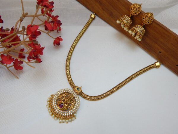 A traditional temple jewelry short necklace with a snake chain and a round goddess pendant with cubic zirconia stones and a single pearl drop.