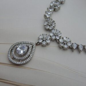 Close-up of the Varsha designer necklace and earring set in a silver tone, featuring floral and teardrop designs with clear, sparkling stones.