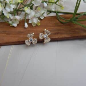 A pair of small, gold-toned huggie hoop earrings with a bow design, featuring a central round stone and baguette-cut stones.