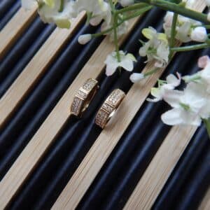 A pair of small, gold-toned huggie hoop earrings with a rectangular shape and rows of clear studs