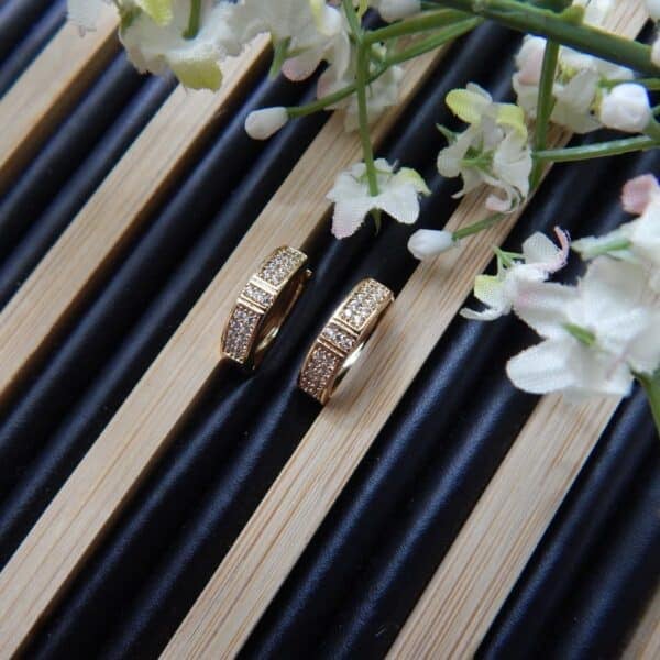 A pair of small, gold-toned huggie hoop earrings with a rectangular shape and rows of clear studs