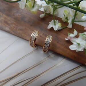 A pair of small, gold-toned huggie hoop earrings with a rectangular shape and rows of clear studs