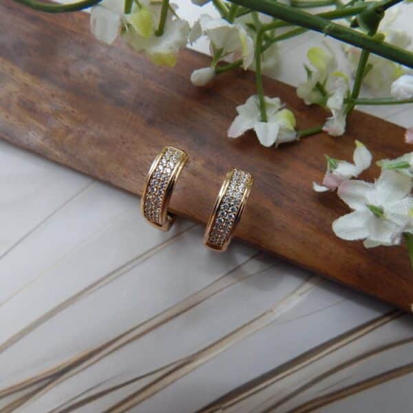 A pair of small, gold-toned huggie hoop earrings with a rectangular shape and rows of clear studs