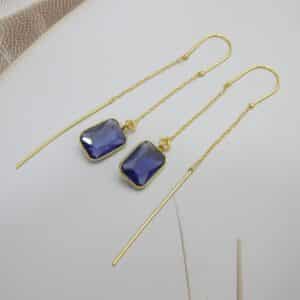 Long gold threader earrings with a hanging blue/violet rectangle cut stone.