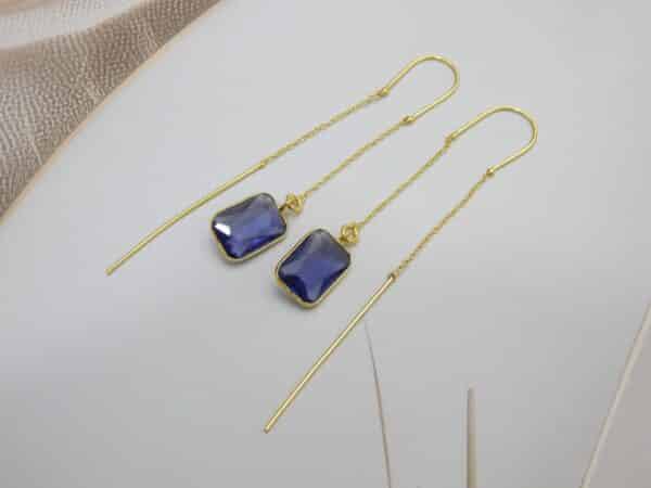 Long gold threader earrings with a hanging blue/violet rectangle cut stone.