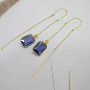 Long gold threader earrings with a hanging blue/violet rectangle cut stone.