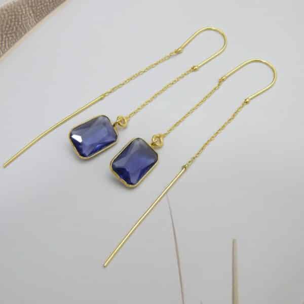 Long gold threader earrings with a hanging blue/violet rectangle cut stone.