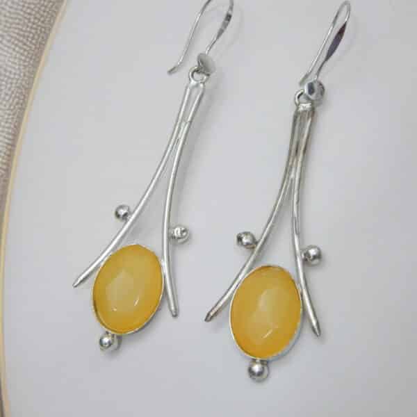 A pair of long, silver-toned earrings with a bohemian design, featuring a large, oval-shaped yellow stone at the bottom and a hook closure.