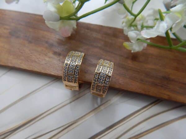 A pair of small, gold-toned huggie hoop earrings with a wide, studded grid pattern.
