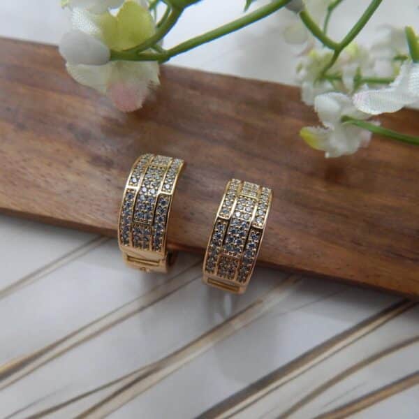 A pair of small, gold-toned huggie hoop earrings with a wide, studded grid pattern.