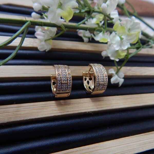 A pair of small, gold-toned huggie hoop earrings with a wide, studded grid pattern.