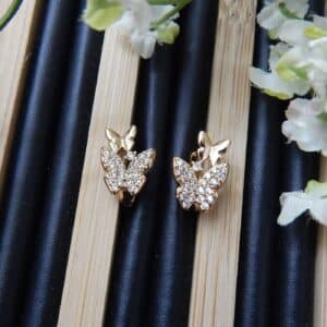 A pair of small, gold-toned huggie hoop earrings with a studded butterfly design.