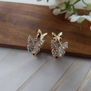 A pair of small, gold-toned huggie hoop earrings with a studded butterfly design.