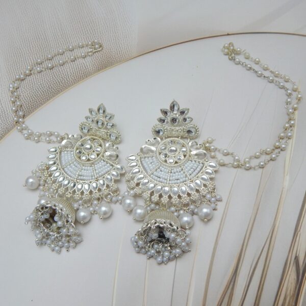 A pair of silver-toned bridal jhumka earrings with an intricate design, adorned with pearls and an attached pearl chain.