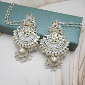 A pair of silver-toned bridal jhumka earrings with an intricate design, adorned with pearls and an attached pearl chain.