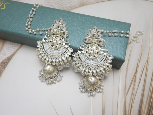 A pair of silver-toned bridal jhumka earrings with an intricate design, adorned with pearls and an attached pearl chain.
