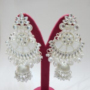 A pair of silver-toned bridal jhumka earrings with an intricate design, adorned with pearls and an attached pearl chain.