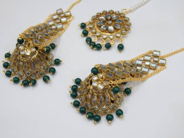 A Kundan maang tikka and matching earrings set with large fan-shaped pendants and dark green beaded drops.