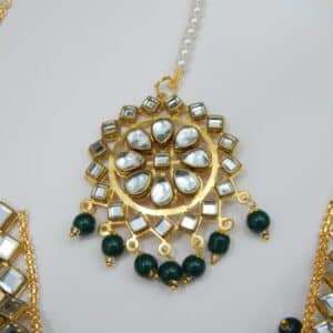A Kundan maang tikka and matching earrings set with large fan-shaped pendants and dark green beaded drops.